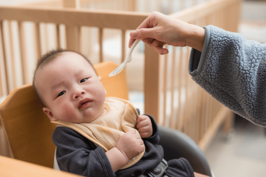 妈妈用汤匙喂坐在餐椅上的宝宝——「追着喂饭」是很多新手妈妈走过的路，但越追往往越糟